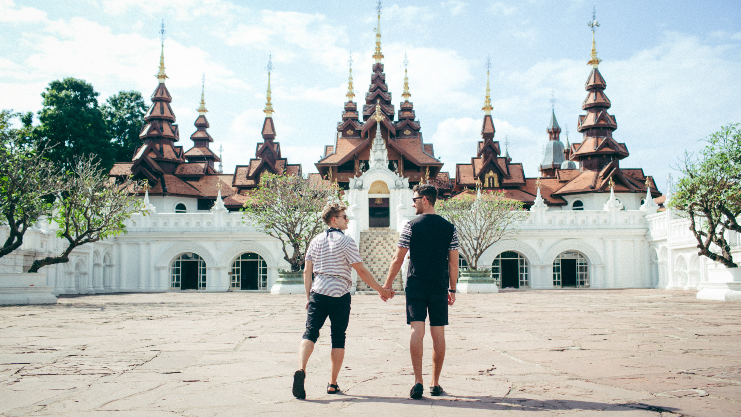 Andrew Keenan-Bolger and Scott Bixby holding hands outside an ornate Thai-style building